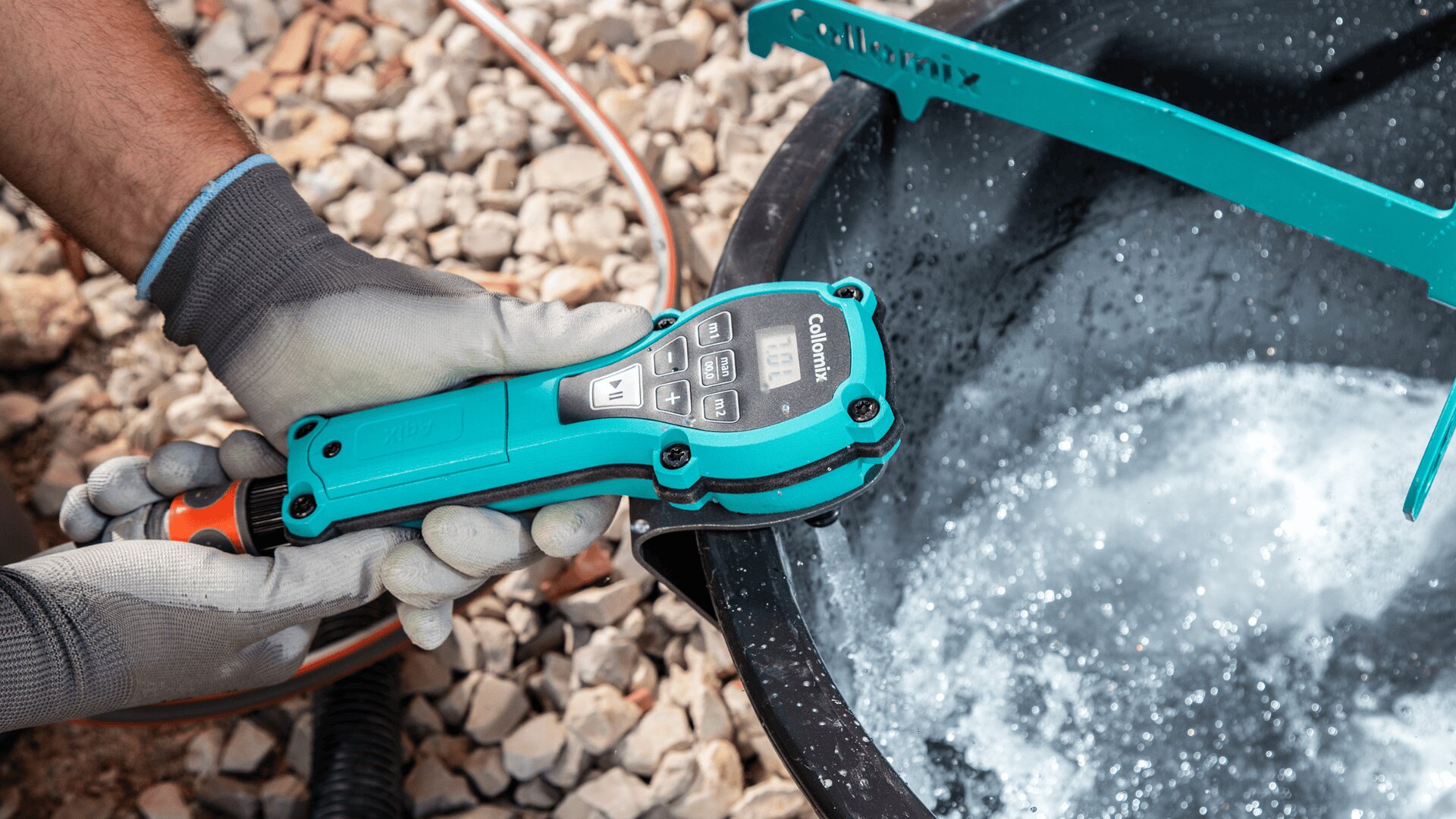 Eine behandschuhte Person hält ein digitales Wassertestgerät über einen schwarzen Behälter mit sprudelndem Wasser; im Hintergrund sind Kies und Schläuche zu sehen.