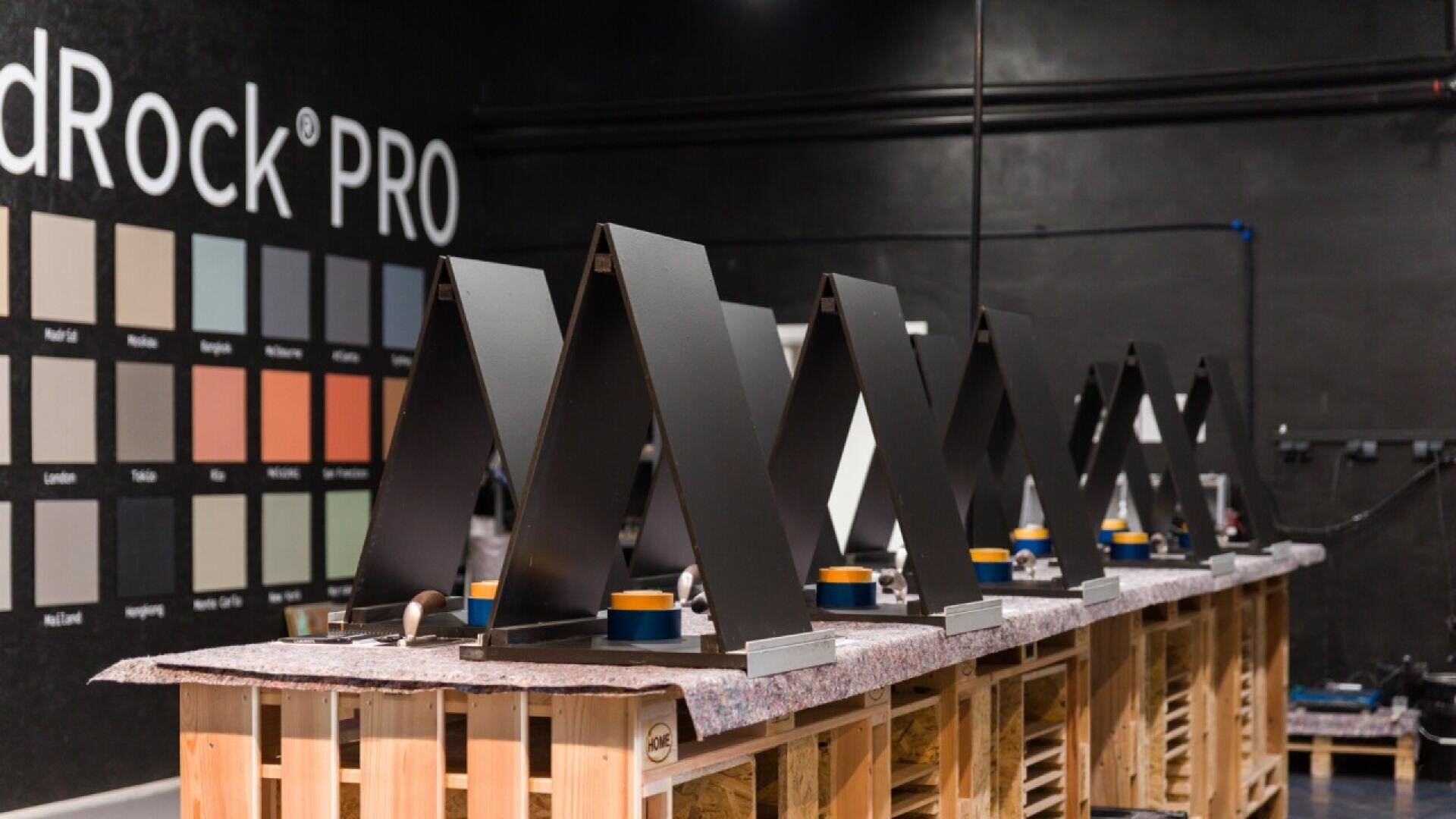 A row of metal range hoods is displayed on wooden pallets in a workshop, with a color sample chart and “RedRock PRO” on the wall in the background.