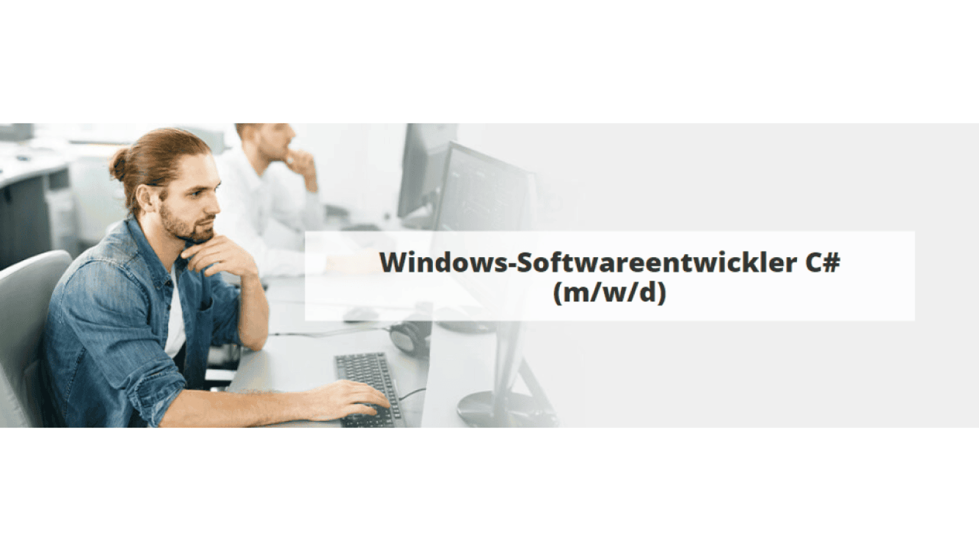 A man with a bun works at a computer in an office. Text over the image reads: Windows-Softwareentwickler C# (m/w/d). Another person sits at a desk in the background.