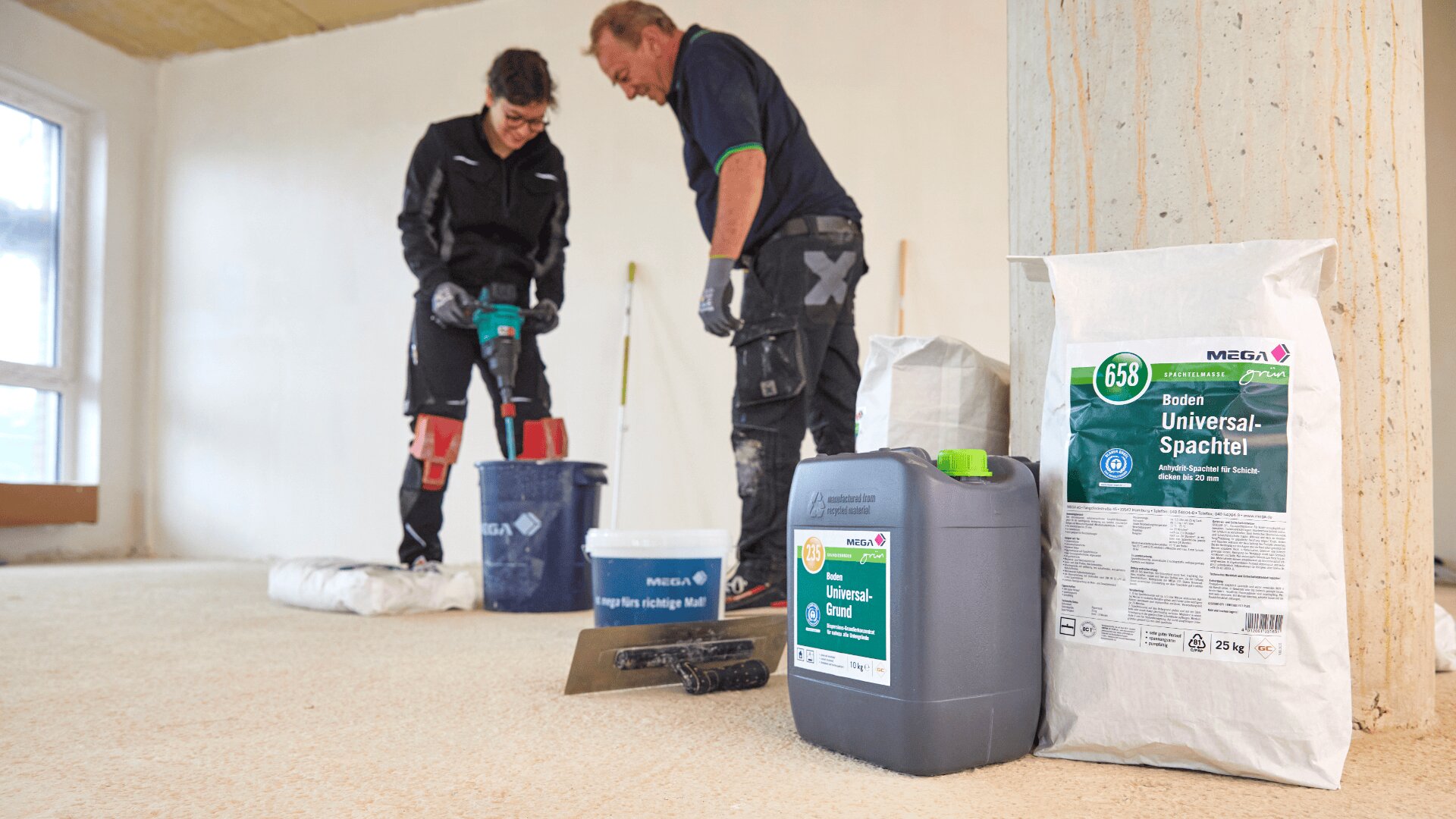 Zwei Personen in Arbeitskleidung mischen in einem renovierten Raum Baumaterial in einem Eimer. Im Vordergrund stehen Säcke und ein Behälter mit der Aufschrift „Universalgrundierung und Spachtelmasse“. Der Raum hat blanke Böden und unbehandelte Wände.