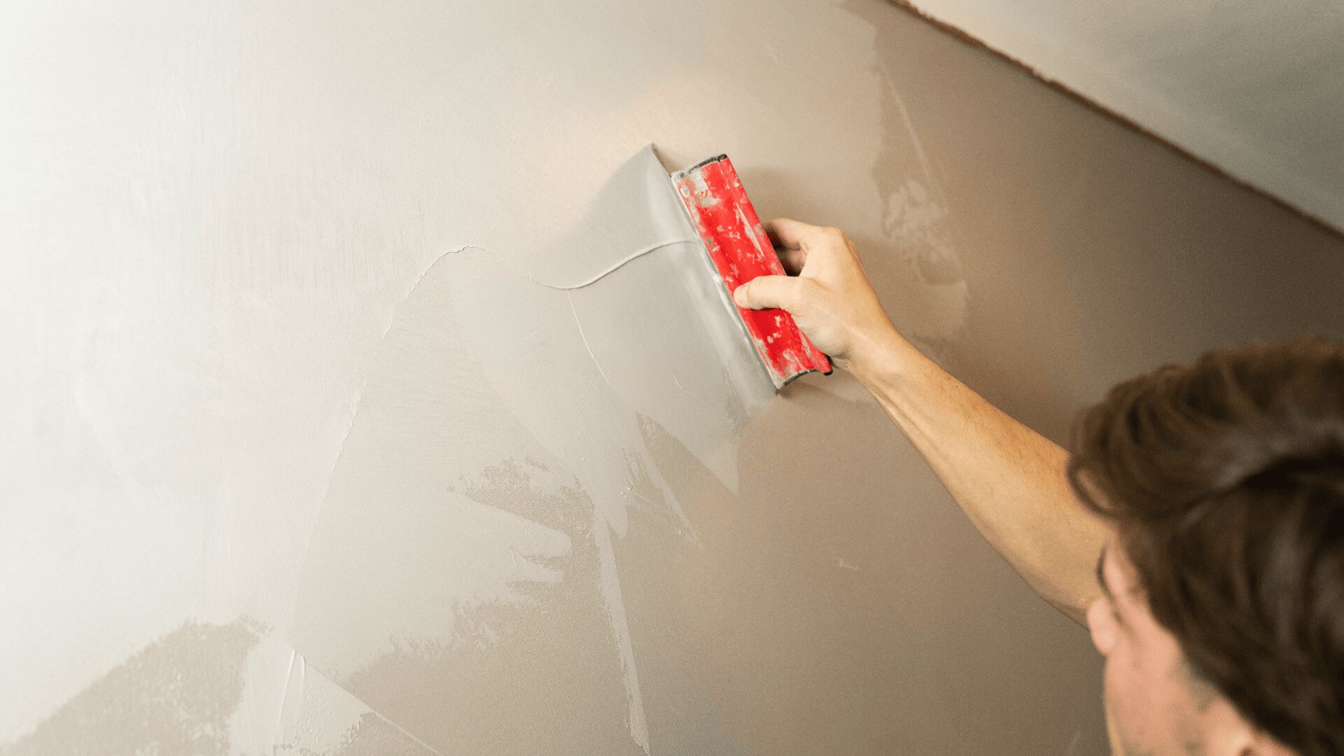 Eine Person verwendet ein rotes Putzwerkzeug, um eine Wand zu glätten und Putz aufzutragen und so die Oberfläche für das Streichen oder die Endbearbeitung vorzubereiten.