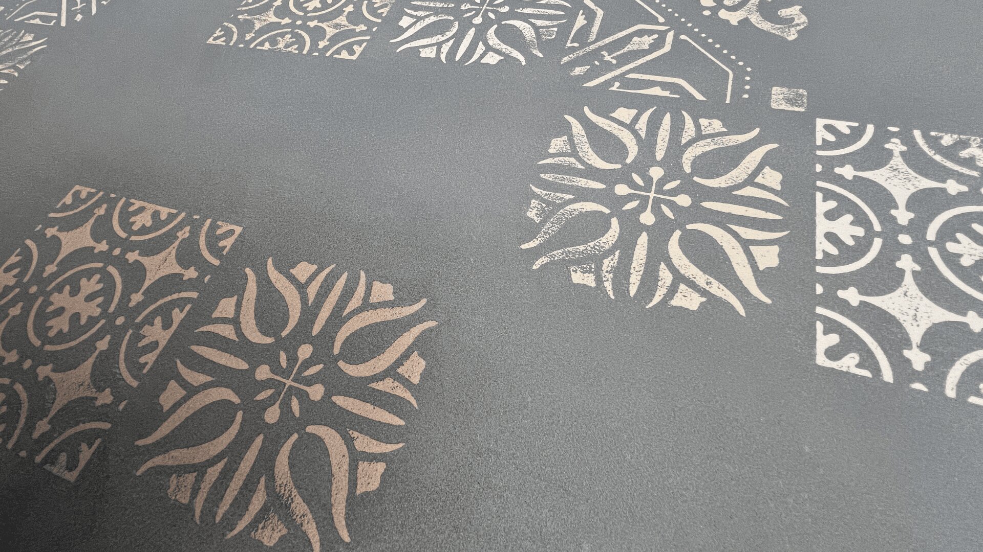 Close-up of a textured surface with a matte gray background, featuring various light-colored floral and geometric tile patterns arranged in a scattered, decorative layout.