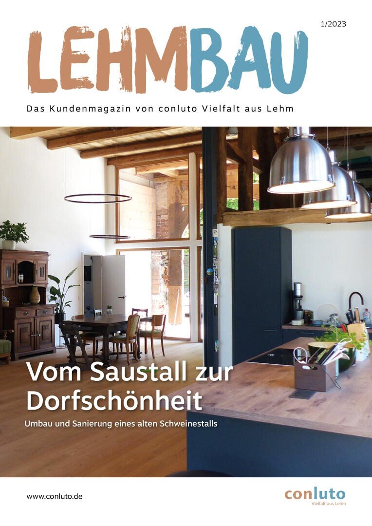 Das Cover einer Zeitschrift mit dem Titel LEHMBAU zeigt eine moderne Küche und einen Essbereich mit Holzbalken, großen Fenstern und Hängelampen. Der Text unten lautet: Vom Saustall zur Dorfschönheit – Umbau und Sanierung eines alten Schweinestalls.