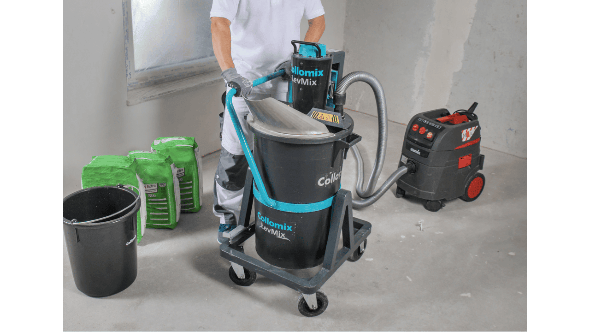 A person using a Collomix LevMix mixing machine in a construction setting, with green bags of material, a black bucket, and a vacuum system nearby on a gray concrete floor.