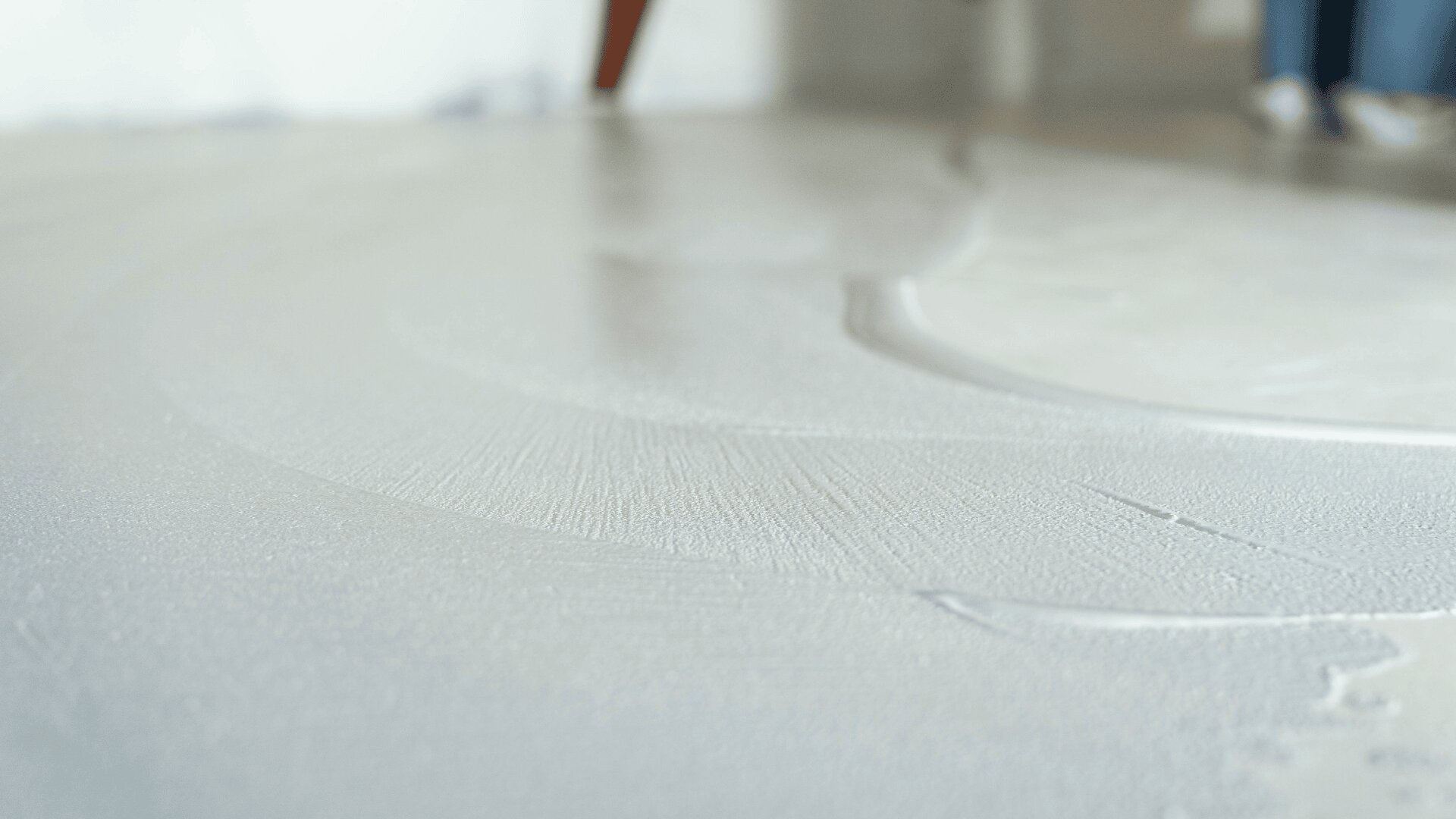 Nahaufnahme einer weißen Substanz, die gleichmäßig auf einer flachen Oberfläche verteilt wird, möglicherweise Gips oder Farbe, mit schwachen Streifen und einem verschwommenen Hintergrund.