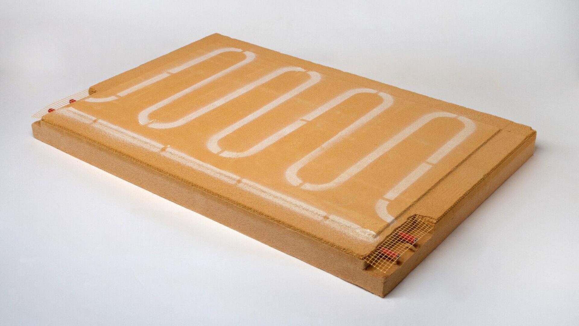 A rectangular panel with a light brown surface features a white, curving tube embedded in an S-shaped pattern, partially visible and framed by mesh at the corners, all set against a plain white background.