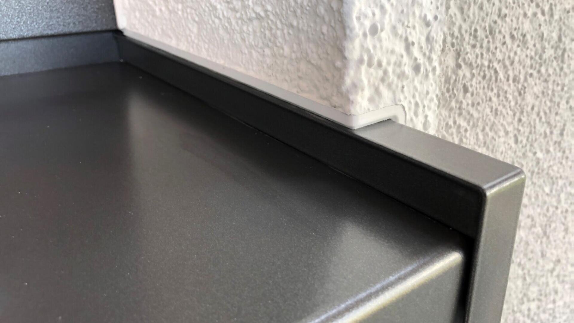 Close-up of a metal shelf with a corner notch cut out to fit around a textured, white-painted wall feature. The shelf is flush against the wall, showing precise alignment and craftsmanship.