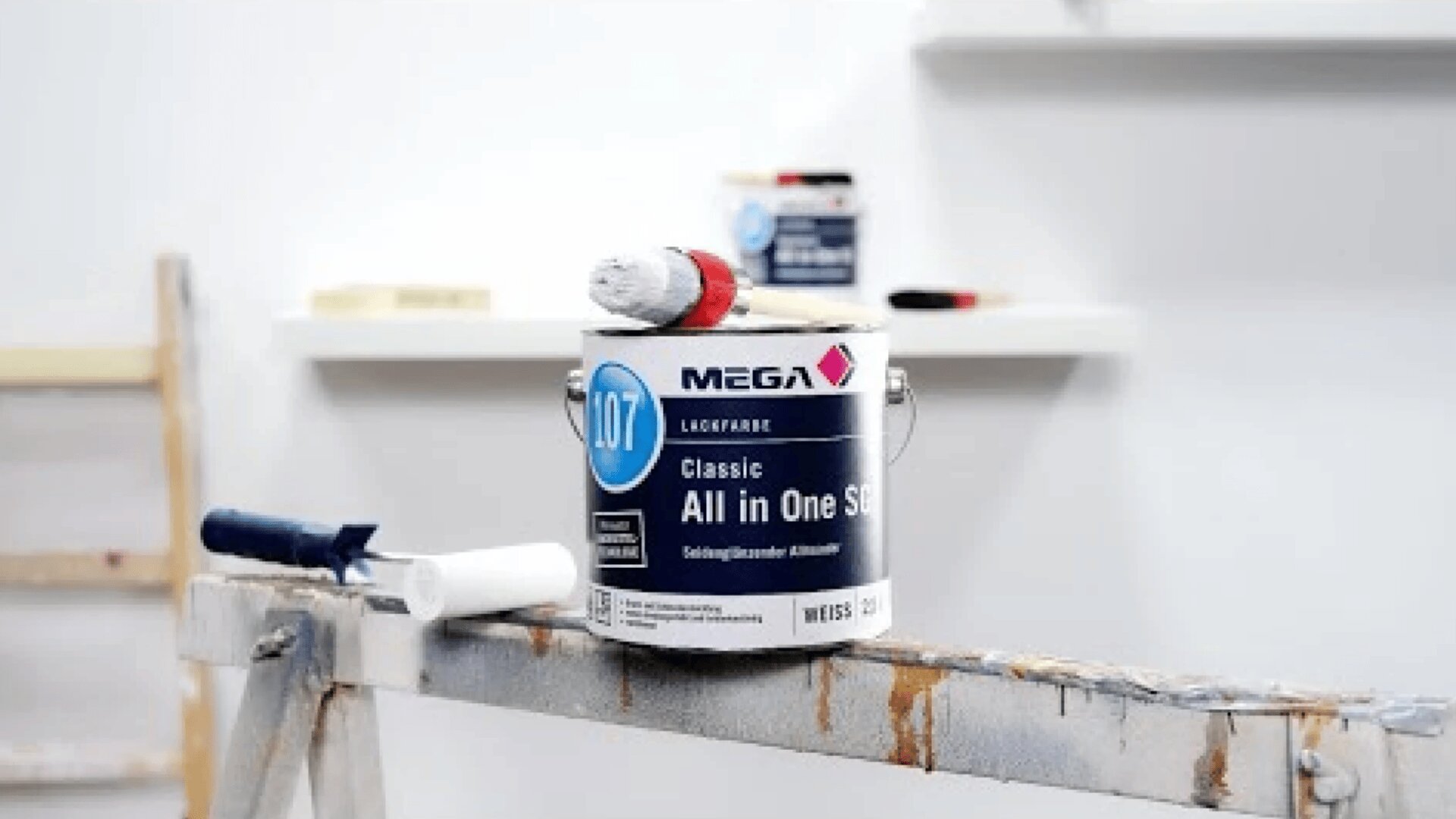 Eine Dose MEGA All-in-One-Farbe mit einem rot-weißen Pinsel darauf, platziert auf einem hölzernen Sägebock. Eine weitere Farbdose und Werkzeuge sind unscharf im Hintergrund zu sehen.