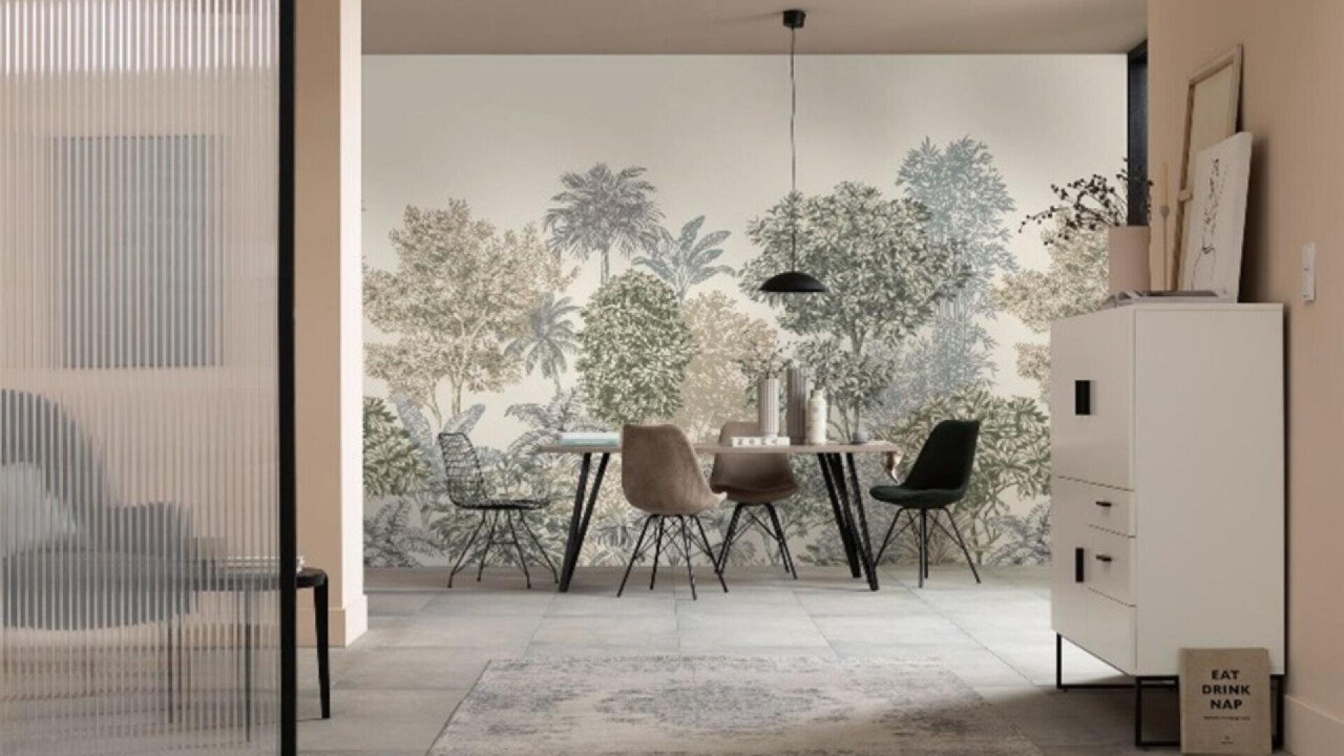 A modern dining area with a table and four mismatched chairs, set against a wallpaper mural of trees. Minimalist décor includes a pendant lamp, framed art, and neutral-toned walls and floor.