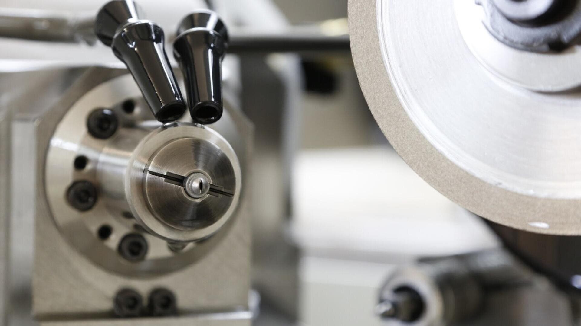 Close-up of a metal lathe machine with a rotating chuck and clamping jaws, showing detailed mechanical parts and precision engineering components in a workshop setting.
