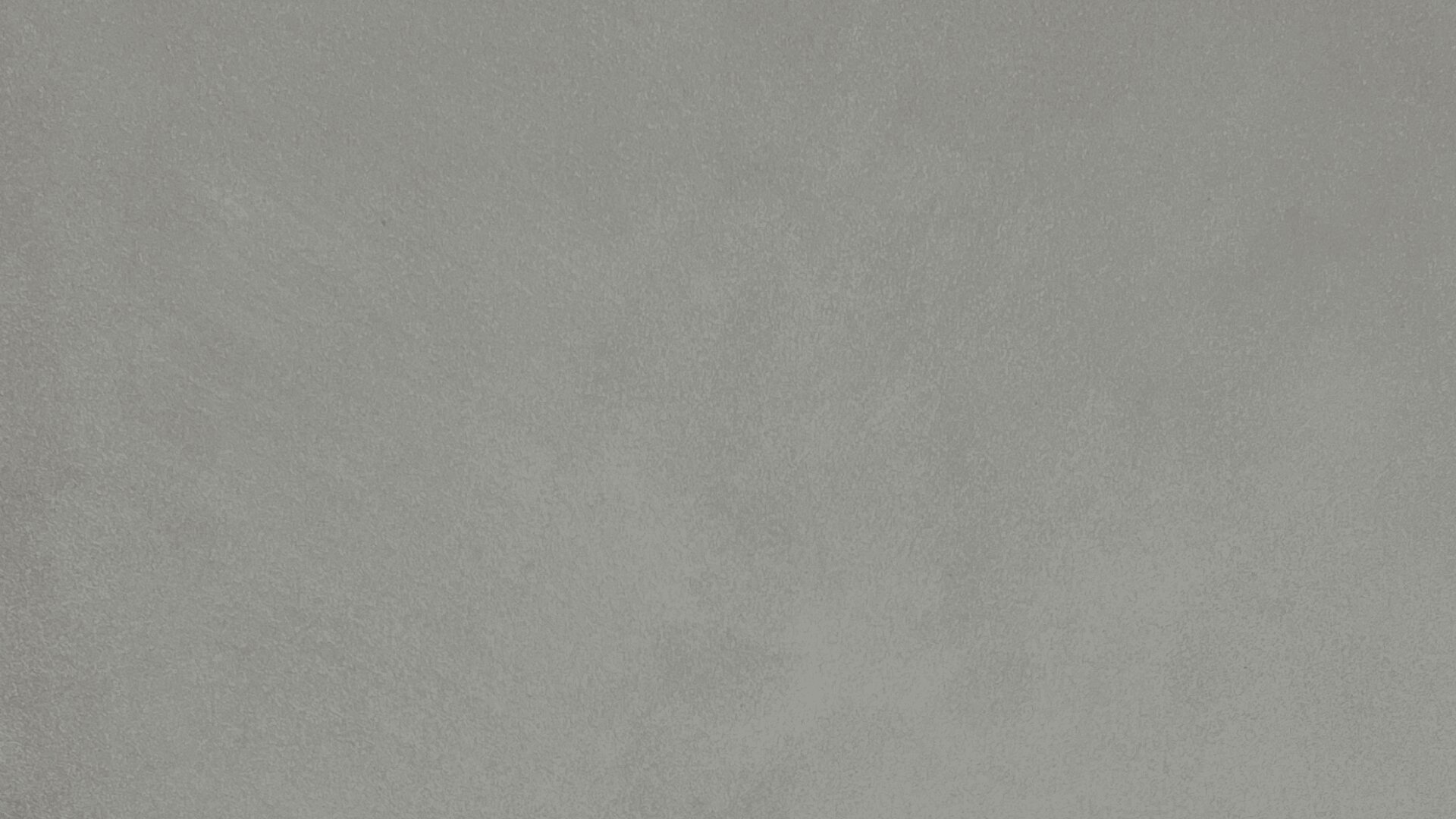 A textured gray concrete surface with subtle variations in tone, creating a slightly rough and mottled appearance.
