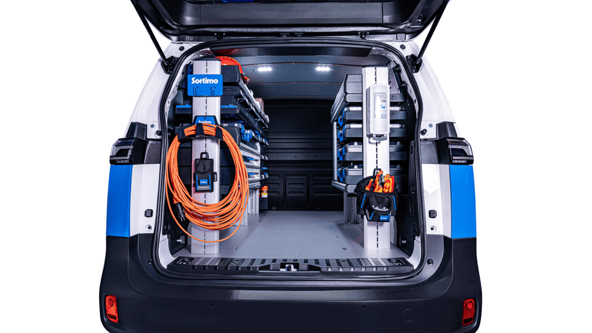 The image shows the organized interior of a utility van with shelving units on both sides, holding tools and equipment. An orange extension cord is neatly wound and hung on the left, and various items are stored along the shelves.