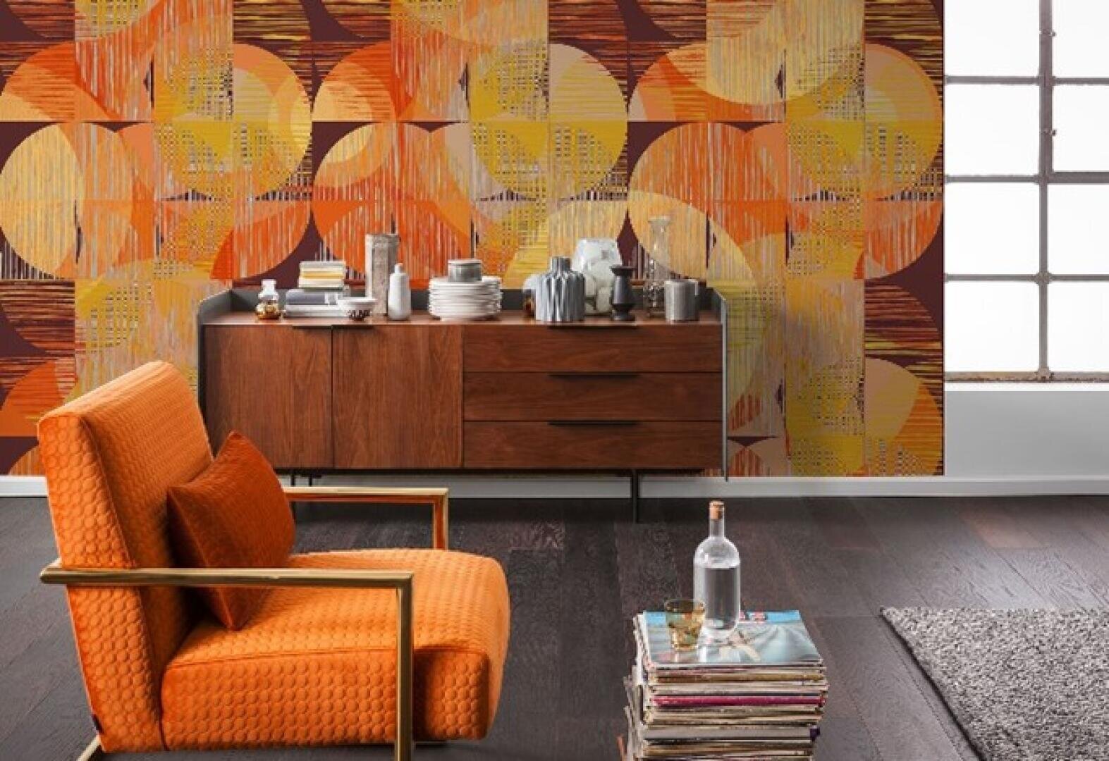 Ein modernes Wohnzimmer im Retro-Stil verfügt über einen orangefarbenen Sessel, ein hölzernes Sideboard mit Geschirr und Kaffeezubehör, einen Stapel Bücher mit einer Glasflasche und eine Tapete mit einem kräftigen orange-gelben geometrischen Muster.