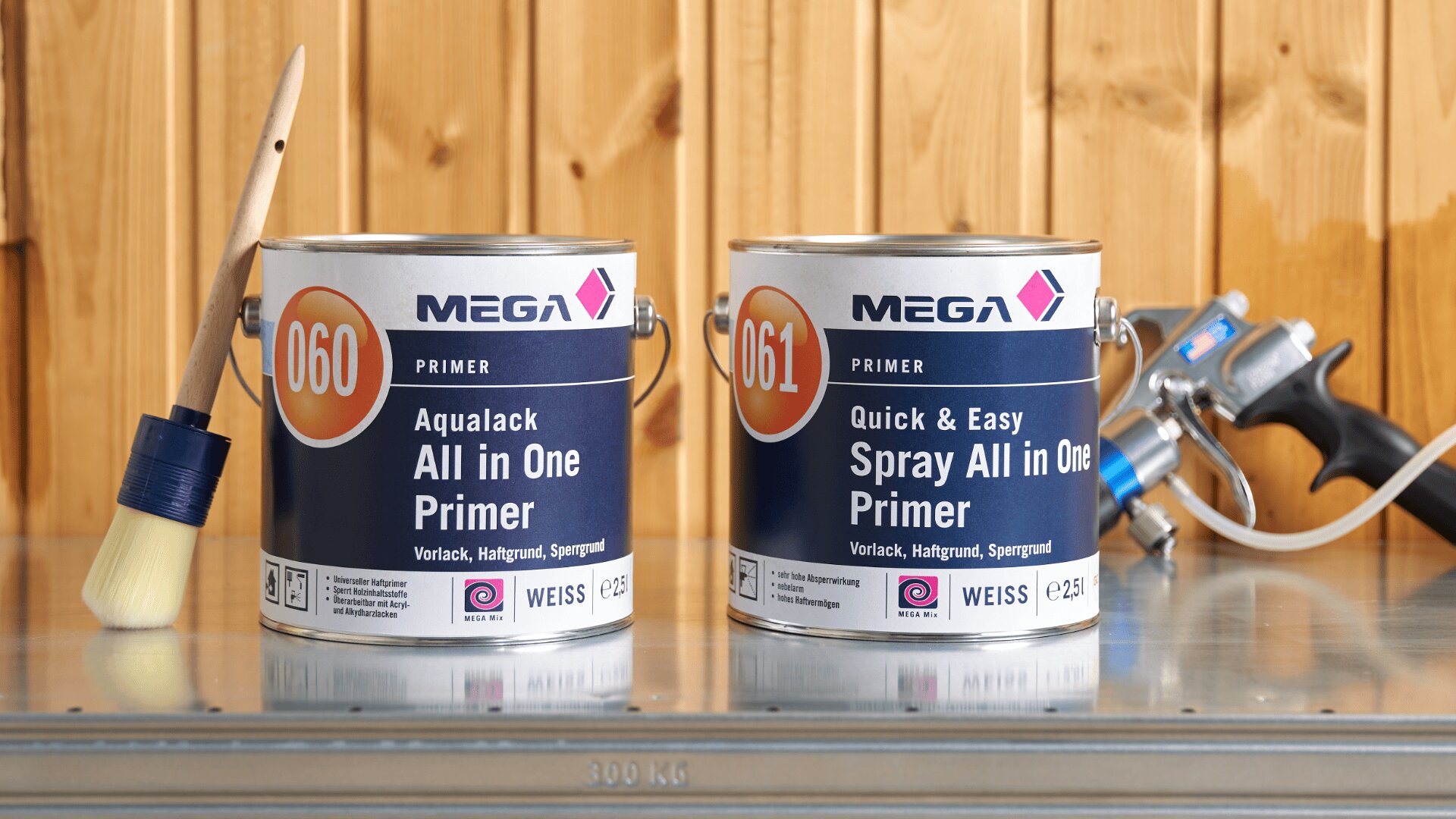 Zwei Dosen MEGA-Grundierung, ein Pinsel und eine Spritzpistole stehen auf einer Metallfläche vor einer Holzwand. Die Dosen tragen die Aufschriften „Aqualack All in One Primer“ und „Quick & Easy Spray All in One Primer“.