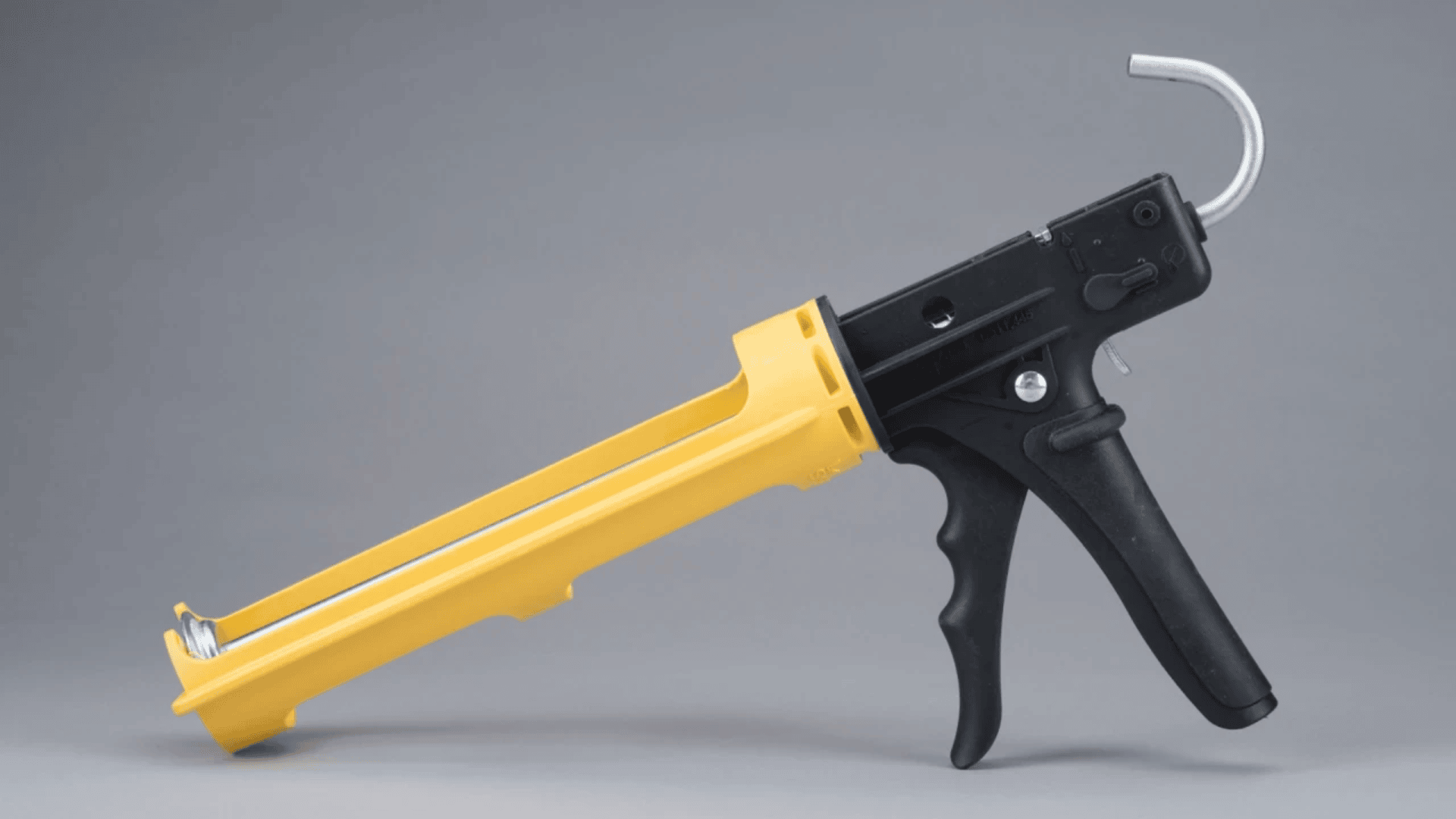 A yellow and black caulking gun is shown on a gray background, positioned horizontally with the handle and trigger facing to the right.