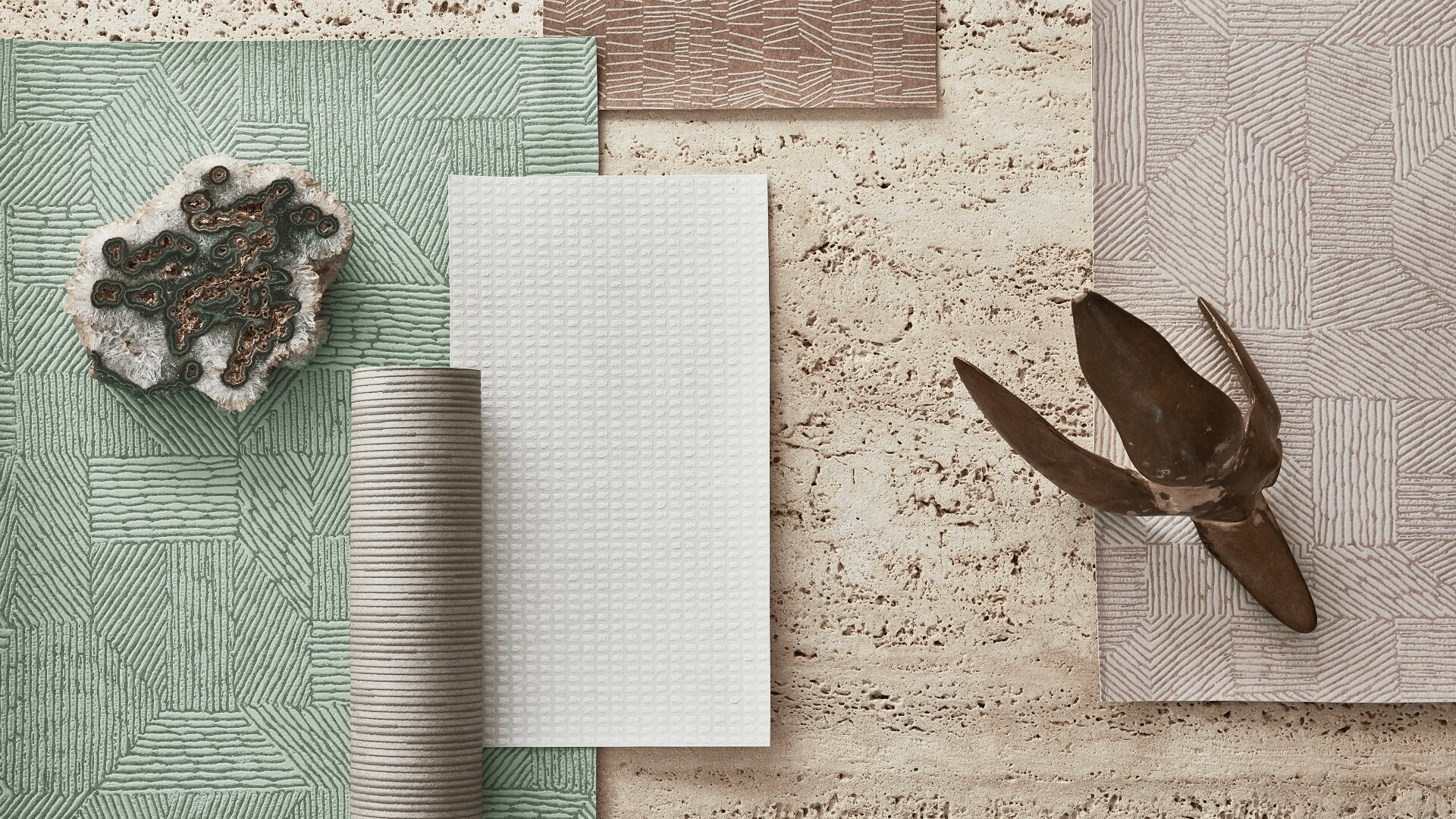 Eine flache Lage strukturierter Stoffe und Fliesen in Erdtönen, darunter Grün, Beige und Weiß; ein Stein mit dunklen Mineraladern; ein gerollter Stoff; und eine abstrakte Metallskulptur auf einer Steinoberfläche.