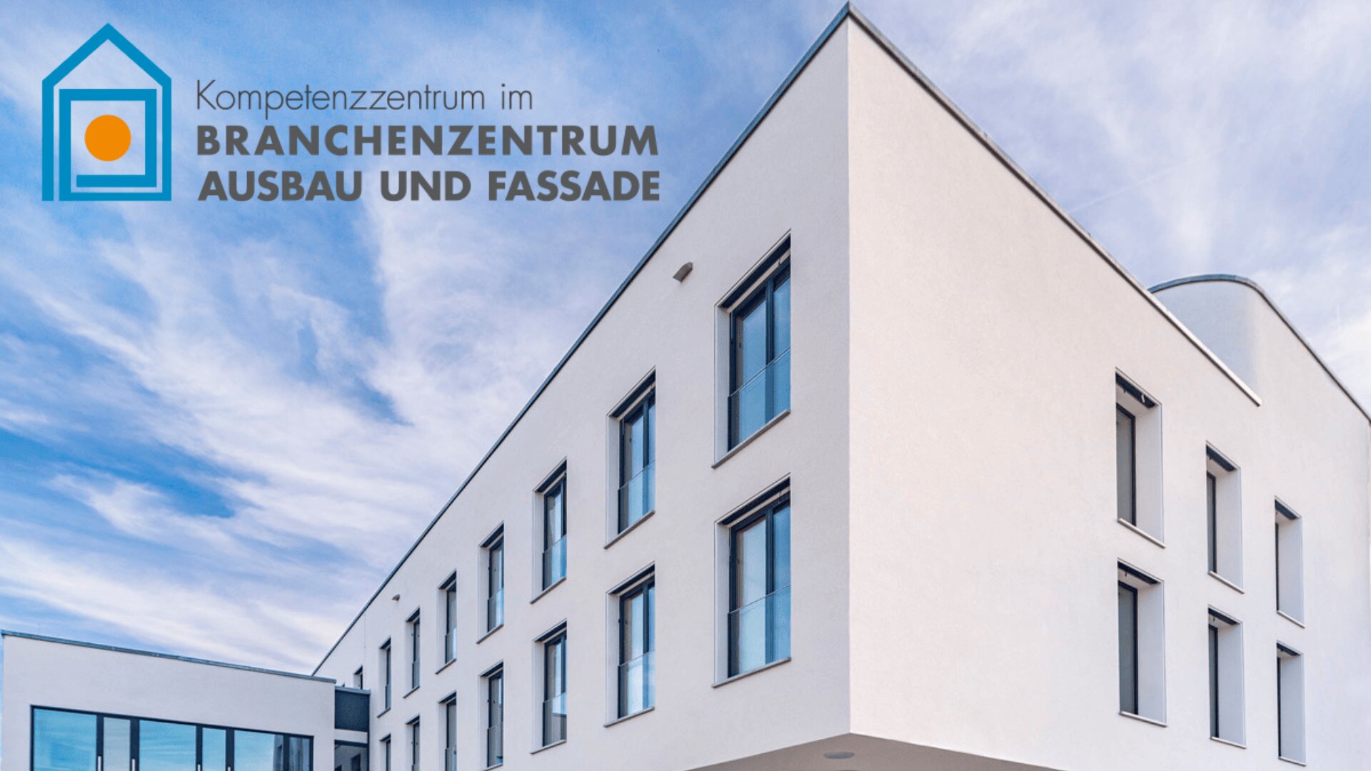 Modernes weißes Gebäude mit großen Fenstern vor blauem Himmel, mit einem Logo und dem deutschen Text „Kompetenzzentrum im Branchzenzentrum Ausbau und Fassade“ in der oberen linken Ecke.