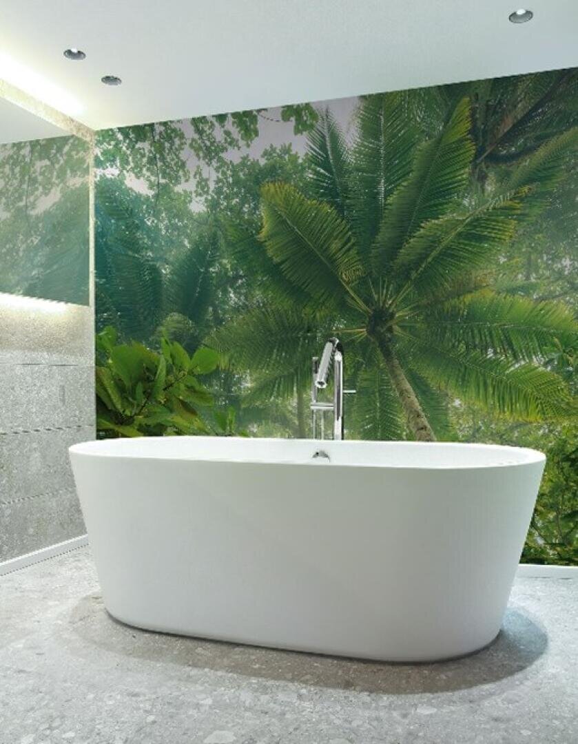 Eine moderne weiße Badewanne steht auf einem Steinboden vor einer Wand, die mit einem großen Wandgemälde aus üppigen grünen Palmenblättern dekoriert ist und im Badezimmer eine tropische Atmosphäre schafft.