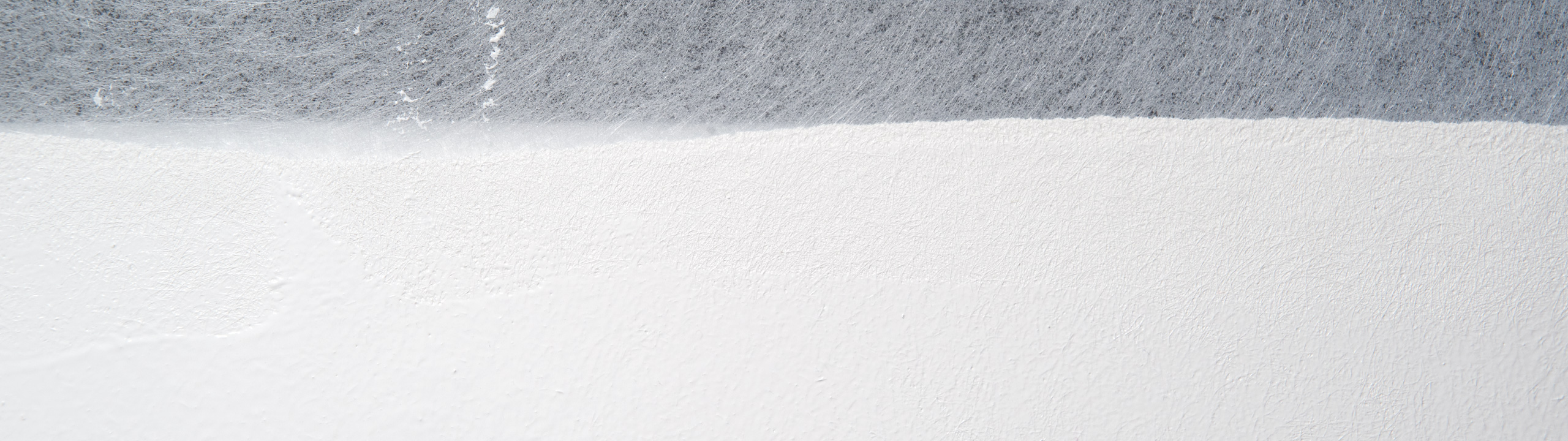 Nahaufnahme einer strukturierten Oberfläche mit einem horizontalen Farbverlauf von Dunkelgrau oben zu strahlendem Weiß unten, der an Papier- oder Stoffschichten mit feinen Fasern und Rauheiten erinnert.